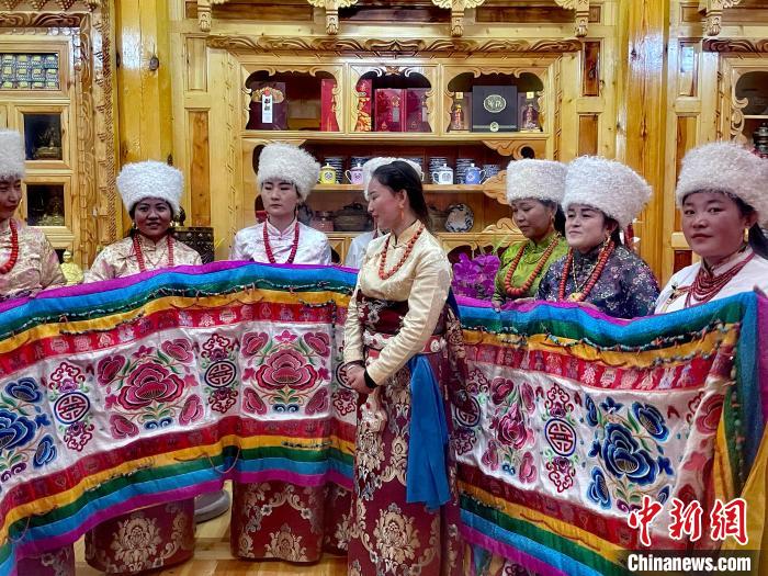 圖為女性展示村民自發(fā)繡制的“百米五彩哈達(dá)”。　李玉峰 攝